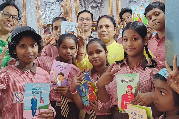 School children holding educational books and smiling with volunteers from Shail-Satya Foundation during a learning program promoting reading and education in India.