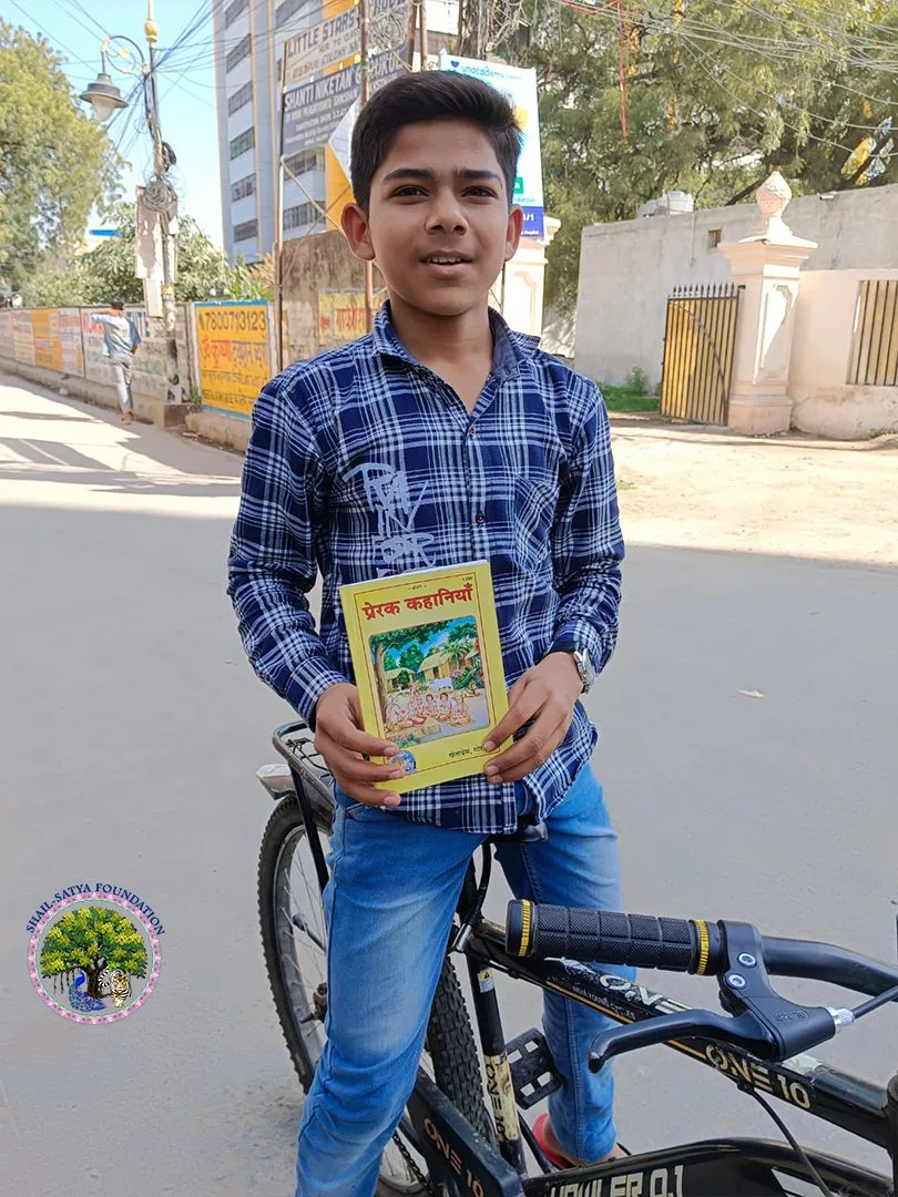 A boy with a bicycle holding the book Prerak Kahaniya