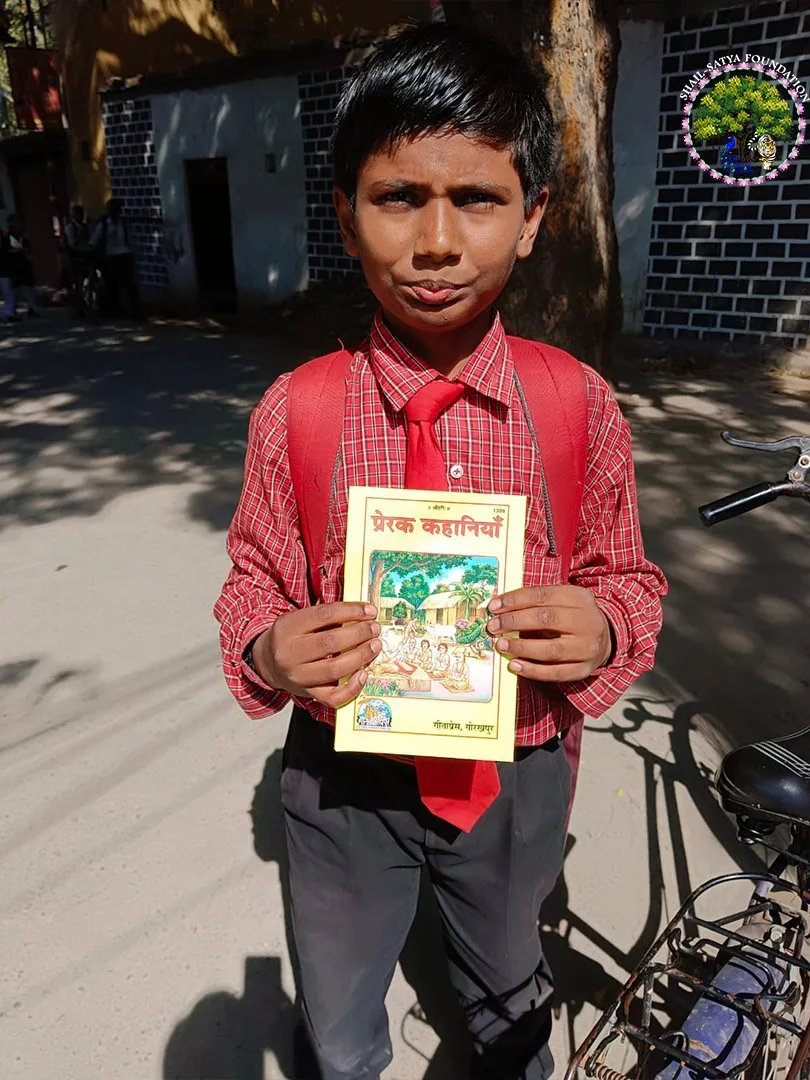 A schoolboy in a red checked shirt showing the book Prerak Kahaniya