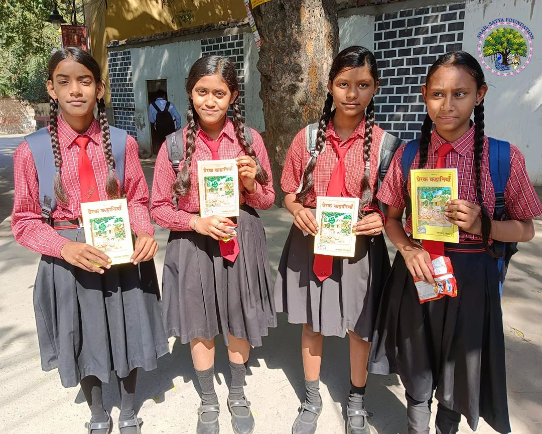 Four students in red shirts holding the book Prerak Kahaniya