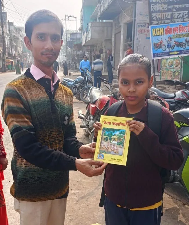 A volunteer handing a copy of Prerak Kahaniya to a student